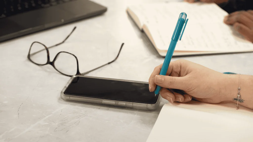 Hand holding a teal coloured pen writing notes for business IT plans in a notebook