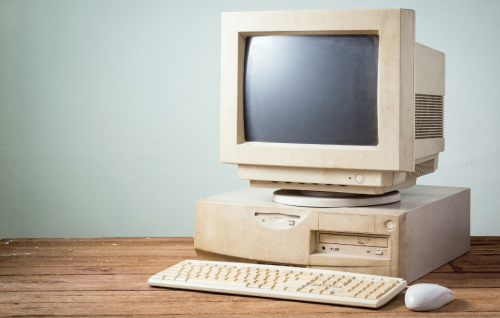 Old and outdated IT system sat on a wooden desk with keyboard and mouse with a light teal/grey wall behind