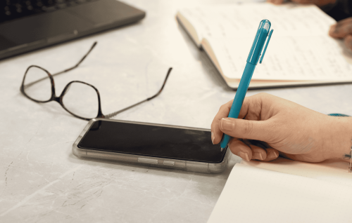 Hand holding a teal coloured pen writing notes for business IT plans in a notebook
